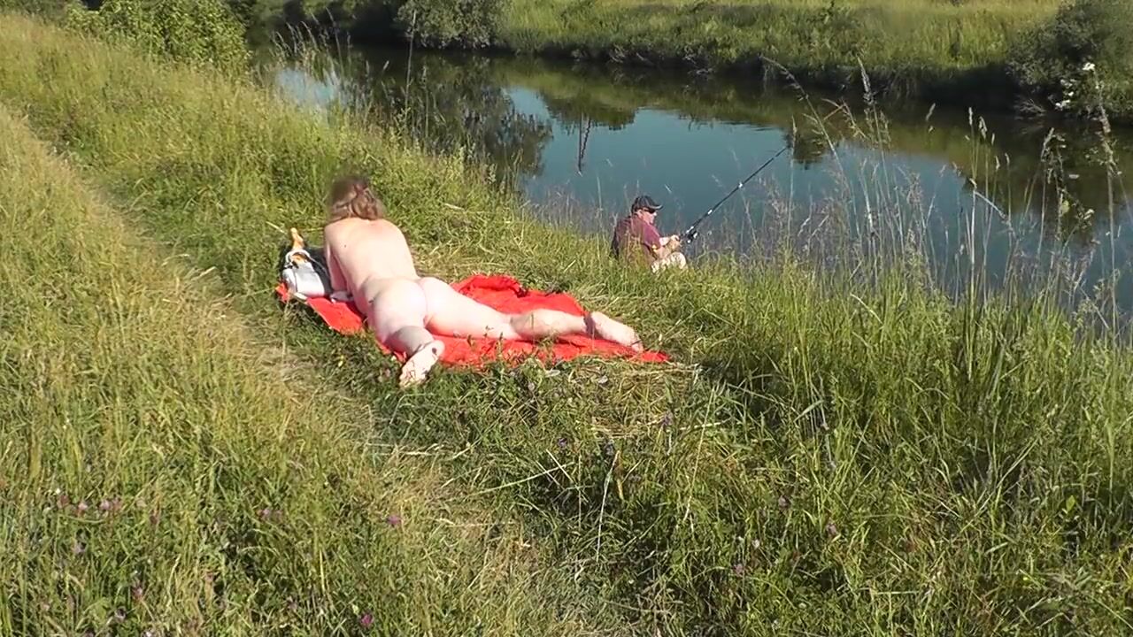 Wild beach. Sexy MILF Platinum naked sunbathing on river bank, random fisherman guy watches